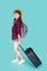 Beautiful young asian woman pulling suitcase isolated on blue background, asia girl having expressive