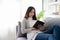 Beautiful young Asian woman reading on a sofa near the window larger