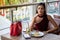 Beautiful young asian woman in red dress sitting in the restaurant looking out the window . elegant lady sitting on table thinking