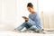 Beautiful young Asian woman wearing knitted sweater sitting in comfort using tablet at cozy home atmosphere on the white bed.