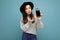 Beautiful young asking dissatisfied brunette woman wearing black hat and grey sweater holding smartphone looking at