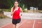 Beautiful young athlete Caucasian woman with big breasts in red T-shirt and short shorts jogging, running in the stadium with red