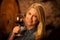 Beautiful young blond woman tasting red wine in a wine cellar
