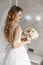 Beautiful young blonde bride with stylish wedding hairstyle in a white fashionable dress with a bouquet of flowers in