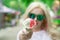 Beautiful, young blonde girl with ice cream in her hands, licks the ice cream on the background of a green park. Italian ice cream