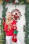 A beautiful young blonde girl in a Santa`s cap stands at the front door decorated with a wreath and branches of spruce