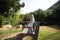 Beautiful young blonde modern dressed woman sitting on a bench in the park with a laptop. The woman is holding an eco-friendly