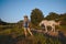 Beautiful young blonde woman dressed safari style in hat and plaid shirt posing with thoroughbreds horses on farm in