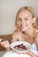 Beautiful young blonde woman eating her oatmeal with berries for breakfast in the morning