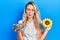 Beautiful young blonde woman holding sunflower seeds an flower making fish face with mouth and squinting eyes, crazy and comical