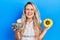 Beautiful young blonde woman holding sunflower seeds an flower smiling and laughing hard out loud because funny crazy joke