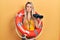 Beautiful young blonde woman wearing bikini and holding lifeguard float and binoculars puffing cheeks with funny face