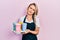 Beautiful young blonde woman wearing waitress apron holding take away cup of coffees skeptic and nervous, frowning upset because