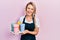 Beautiful young blonde woman wearing waitress apron holding take away cup of coffees smiling and laughing hard out loud because