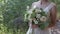 Beautiful young bride holding bridal bouquet of pastel roses, walking in a park.