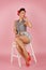 Beautiful young bright girl in retro style pin-up style, sits on a white step ladder on a pink glamorous background