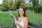 Beautiful young brownhair girl is reading the book and enjoys the smell of a fresh printed book sitting on the bench in the park