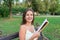 Beautiful young brownhair girl is reading the book and enjoys the smell of a fresh printed book sitting on the bench in the park