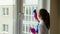 Beautiful young brunette girls stand with their backs and do the cleaning. Girl washes a window with detergent.