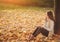 Beautiful young brunette sitting on a fallen autumn leaves in a park, reading a book or write a diary