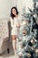 Beautiful young brunette woman standing near fir tree in Christmas decorated room.
