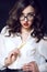 Beautiful young business woman with dark wavy hair and red lips wearing white silk blouse looking direct over her glasses
