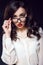 Beautiful young business woman with dark wavy hair and red lips wearing white silk blouse looking straight over her glasses