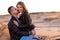 Beautiful young Caucasian couple dressed black leather jacket and blue jeans. A man sits on the sand woman sits on top and hugs
