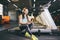 Beautiful young Caucasian girl sportswoman sitting, resting after training on treadmill against the backdrop of gym in sunny weath