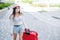 A beautiful young Caucasian woman in a medical mask walks down the street with a red suitcase. A girl with luggage