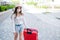 A beautiful young Caucasian woman in a medical mask walks down the street with a red suitcase. A girl with luggage