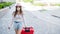 A beautiful young Caucasian woman in a medical mask walks down the street with a red suitcase. A girl with luggage