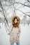 A beautiful young Caucasian woman stands in a snowy park in a jacket with a hood and fur on her head in jeans and holds a pair of