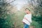 Beautiful young cheerful pregnant woman in wreath of flowers on head touching belly while walking in spring tree garden. Beauty