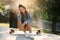 Beautiful young cheerful woman sits on skateboard in urban space at sunrise.