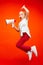 Beautiful young child teen girl jumping with megaphone over red background