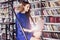 Beautiful young college student sitting on stairs in the library, working on laptop. Woman wearing blue dress, huge bookshelf