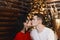 Beautiful young couple, boyfriend wearing sweater and girlfriend in sexy dress kissing in Christmas interior. Young