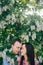 Beautiful young couple gently hugging in green leaves and white flowers in spring garden in sunshine. Happy family embracing at