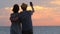 Beautiful young couple looking out for sunrise sunset, making selfie on smartphone. Happy spouse enjoying vacation at