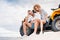 beautiful young couple sitting on ATV on sandy dune and looking