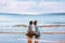 Beautiful young couple sitting on sand in front of each other in sea waves. Young man and woman love story on the beach