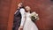 A beautiful young couple stands near the brown wall of a tall building. Lovers smile.