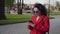 Beautiful young curly girl in a red coat flips through a smartphone in the city