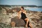 Beautiful young curvy woman in the black dress posing on the stones at sunset. Wild nature, natural beauty