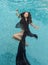 Beautiful young dark-haired woman relaxed in black dress, cape, towel floats happily floating in the pool