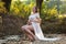Beautiful young expecting women sitting by creek in the park 9 months pregnant wearing white dress