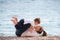 Beautiful young family of lying mother and child wishing to kiss on sea beach in springtime during leisure active outdoor game