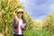 A beautiful young farmer stands holding a corn and smiles happily.