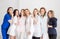 Beautiful young female doctors in white uniforms posing against the background of a white wall. Women hugging as a sign of team